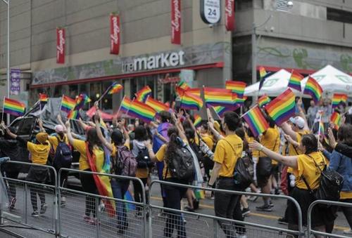 University of Waterloo community members march in the Toronto Pride Parade waving rainbow flags.