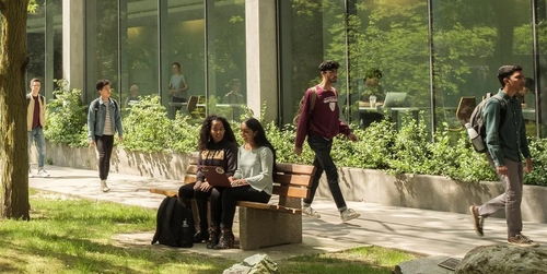 Students walk on campus pathways surrounded by greenery.