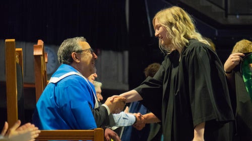 Feridun Hamdullahpur shakes the hand of a graduand on the Convocation stage.