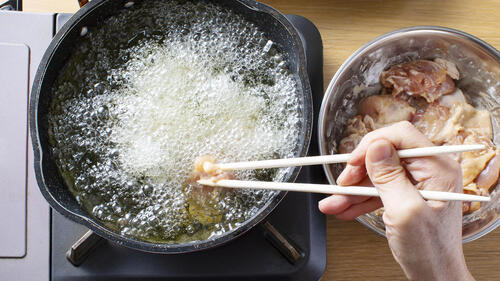 Someone dipping chopsticks holding meat into a bowl of hot oil.