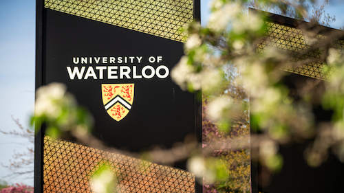 Waterloo signs at the University's south entrance, with tree blossoms in the foreground.