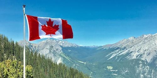 A Canadian flag in the breeze with a mountain in the background.