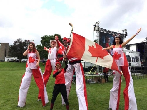 A Canada Day volunteer waves a Canadian flag on a hockey stick with three stilt walkers.