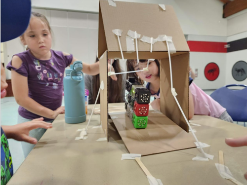 Children interact with the Travelling STEM exhibit making things out of cardboard and drinking straws.