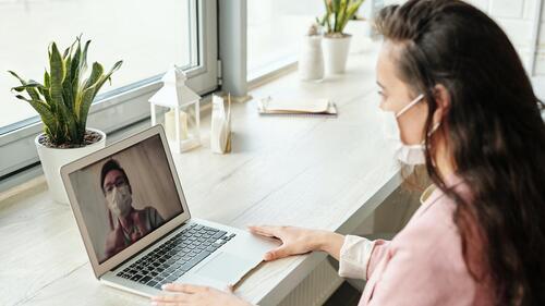 A woman in a mask has a video call with another masked person.