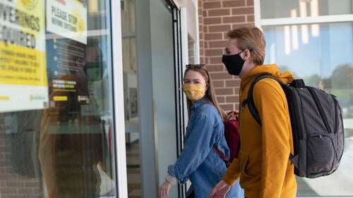 Two masked students walk into a building entrance.