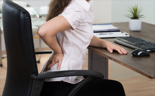 A person presses her hand to her back as she sits at her office desk.
