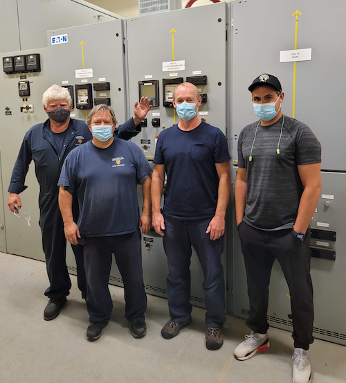Four Plant Operations crew members stand in front of tall power units.
