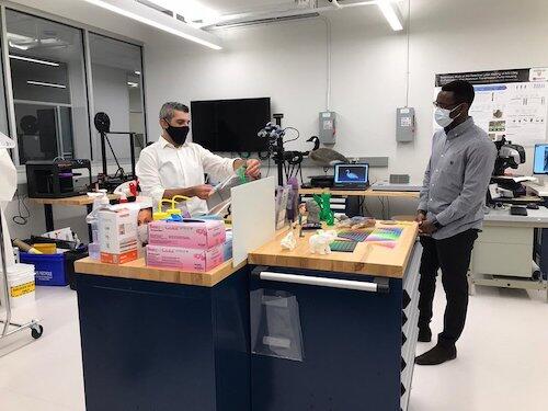 Minister of Colleges and Universities Ross Romano looks at 3D-printed face shields with Francis Dibia, internal and external services coordinator for the Multi-Scale Additive Manufacturing Lab (MSAM).