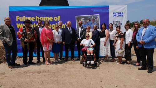 Premier Doug Ford, local political dignitaries and University representatives stand in front of a sign advertising the future site of the hospital.