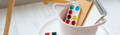 Art supplies in a basket include a palette of paint colours.