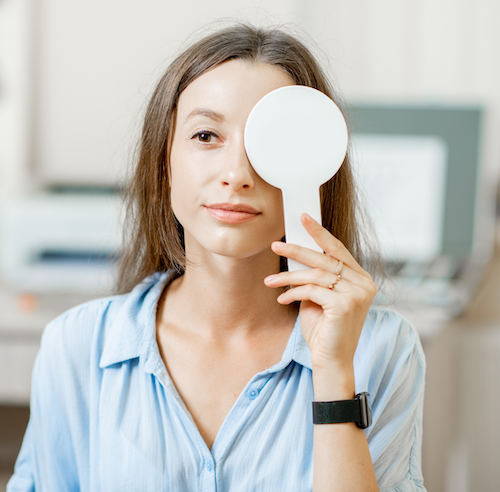 A woman uses a paddle-like object to cover up one of her eyes.