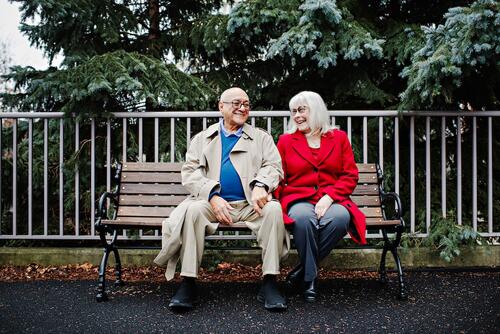 Gil Aburto-Avila and his wife sit on a park bench, smiling.