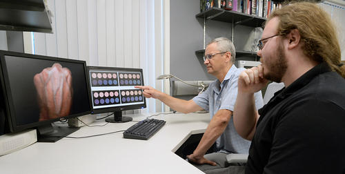 Professor Gladimir Baranoski (left) and his master's student Spencer Van Leeuwen examine computer-generated swatches depicting the effect of Rayleigh scattering in the papillary dermis on the appearance of a skin specimen without (pink circles) and with (blue circles) a subcutaneous vein. The monitor on the left shows the typical distinct contrast of skin appearance caused by subcutaneous veins.