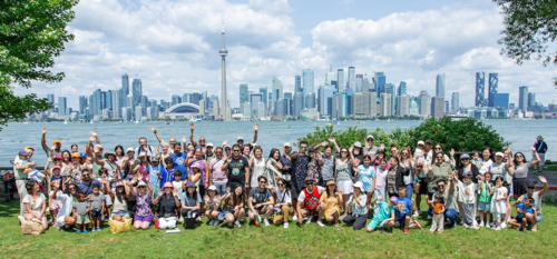 Waterloo alumni and their families pose for a group photo on Toronto Island with the Toronto skyline behind them.