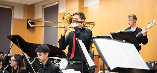 A trombonist stands and performs a solo while the rest of the jazz ensemble plays on.