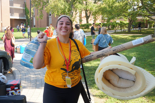 A move-in volunteer smiles as she helps new students with their stuff.