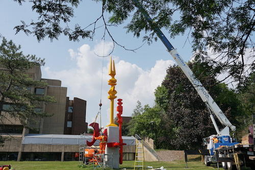 Workers install Ron Baird's painted steel sculptures on a pillar outside the PAS building.