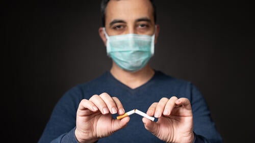 A man in wearing PPE breaks a cigarette in two.