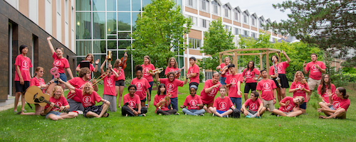 Campers and counsellors in red t-shirts brandish instruments in a group photo.