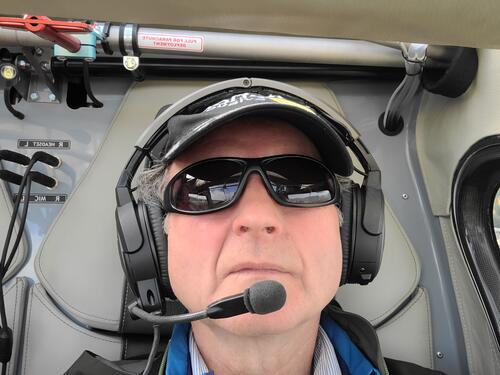 Paul Parker wears a headset and sunglasses while at the controls of an airplane.