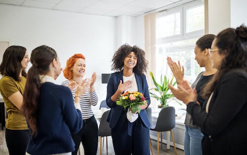 A woman receives a bouqet of flowers from her supportive colleagues.
