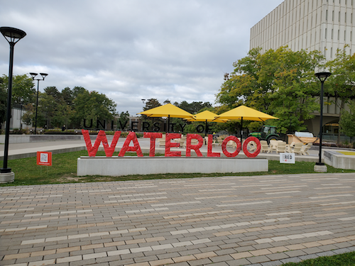 The University of Waterloo sign wrapped in red with the Dana Porter Library in the background.