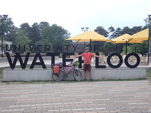 Steven Ekvall with his bike in front of the University of Waterloo sign.