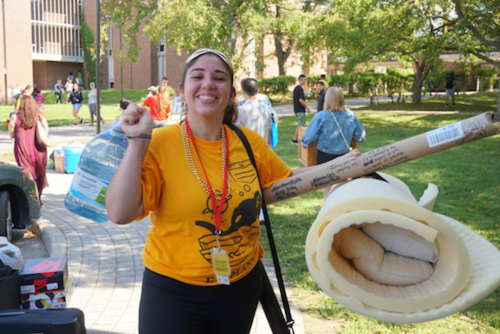 A smiling volunteer helps new students move in.