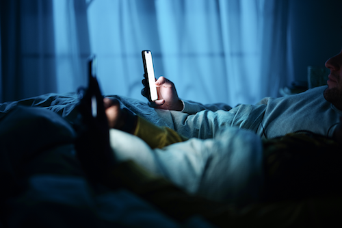 Two people interact with their smartphones while in bed.