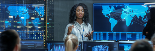 A woman speaks to her colleagues in a computer command centre.