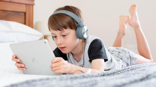 A boy plays with a tablet while wearing headphones.
