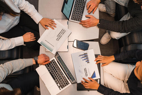 An overhead shot of a conference table - on it are hands, papers and a laptop