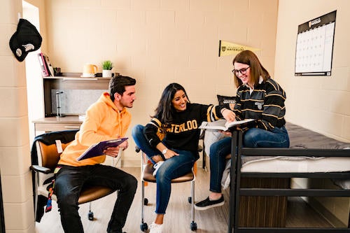Students wearing Waterloo apparel sit in a residence room.