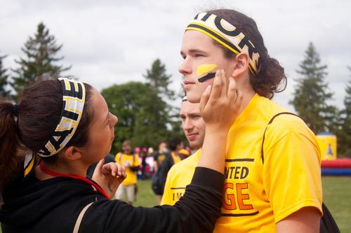 A volunteer applies Warrior facepaint to a student.