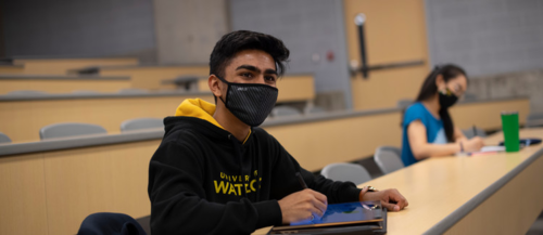 A masked student sits in a lecture hall.