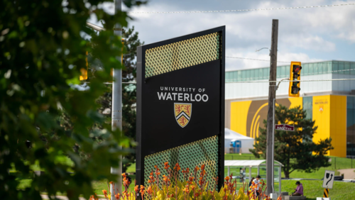 The University of Waterloo's sign at the north campus entrance with the Field House in the background.