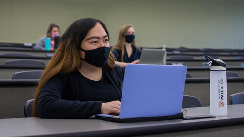 Students wearing masks sit in a lecture hall.