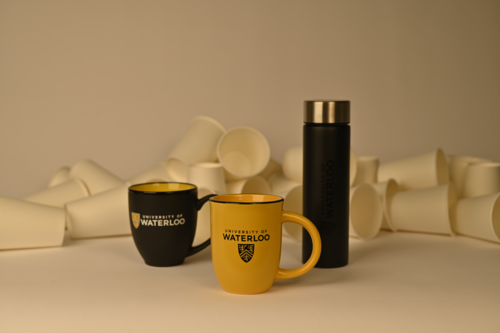 Waterloo-branded coffee mugs and a travel thermos with a pile of paper cups in the background.