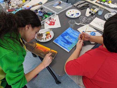 Youth creating pieces during the art camp on February 15, 2020.  Adriana Johnson works on 'drought', one side of a two-sided collaborative paddle work titled of 'Two Points of the Problem' (page 14 in the virtual tour).  Clinton Bomberry-Smith works on his untitled painting on canvas.