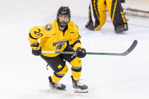 Hockey player Leah Herrfort skates toward the camera pursued by opponents