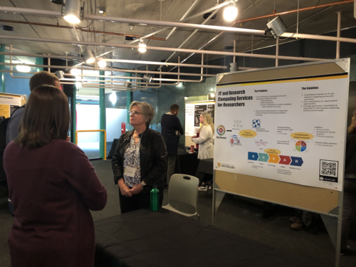 Wendy Hague stands next to a poster presentation board and she interacts with P3 showcase attendees.