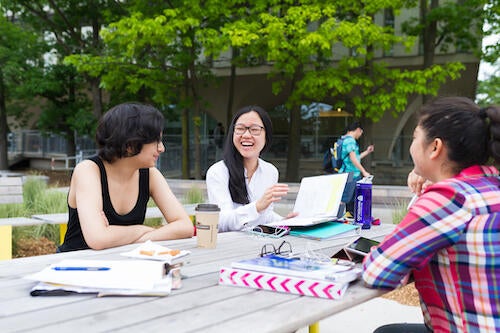 Three students sit at a picnic table on campus.