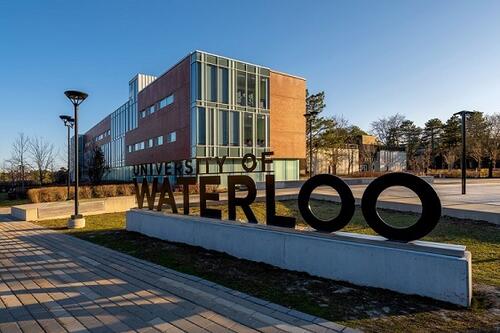 The University of Waterloo sign with the Tatham Centre in the background.