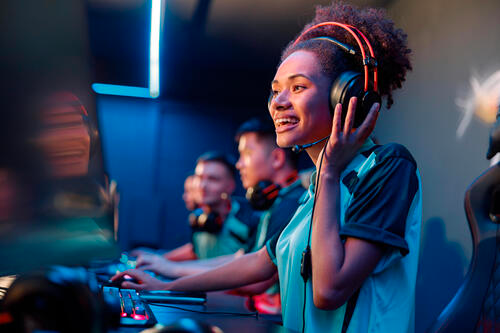 A woman wearing a headset plays eSports with teammates while at a computer.