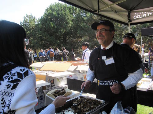 Feridun Hamdullahpur serves food to a student at the President and Senior Staff Luncheon.