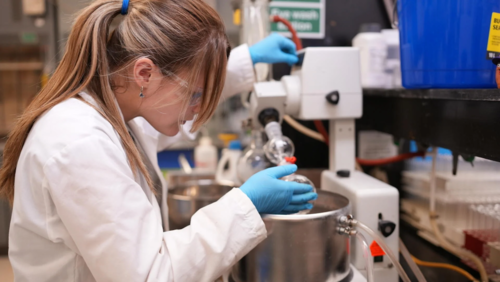 Lindsey Shivers operates lab equipment while wearing protective glasses and a lab coat.