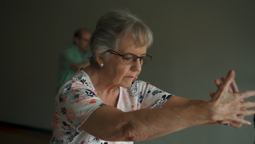 An elderly woman stretches her arms out in front of her.
