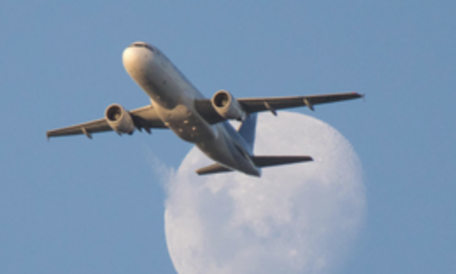 A jetliner flies with the Moon in the background.