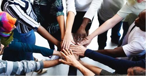 Diverse people put their hands together for a cheer.